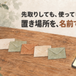 木のテーブルに封筒が5つ並び、そばにスマートフォンが置かれた水彩イラスト。先取りしたお金を名前で分けて置く目的別口座のイメージ
